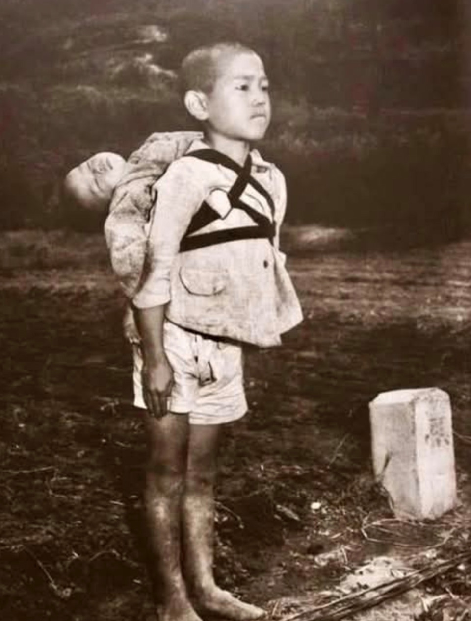 Ez a történelmi fénykép 1945-ben készült Nagaszakiban, nem sokkal azután, hogy 1945. augusztus 9-én atomtámadás érte a várost.Egy körülbelül tízéves kisfiú áll katonás tartásban, és türelmesen várja sorát a halotti máglya előtt, hogy elhamvasszák öccsét, aki a bombázás következtében vesztette életét.A temetési egység egyik katonája észrevette, hogy a fiú kimerült a teher cipelésétől, s javasolta, hogy tegye le a halott gyermeket a földre. A fiú így felelt: „Ő nem nehéz. Nem megterhelő számomra. Ő a testvérem.”A fénykép készítője, Joe O’Donnell emlékirataiban ezt írta: „Egy körülbelül tízéves fiút láttam közeledni. A hátán egy kisgyermeket vitt. Abban az időben Japánban gyakran láttunk gyerekeket, amint kisebb testvéreiket cipelték játékosan a hátukon, de ez a fiú más volt. Éreztem, hogy súlyos ok húzódik meg jelenléte mögött. Mezítláb volt. Arca megkeményedett, szinte kővé vált. A kisgyermek feje ide-oda billegett, mintha aludna. A fiú öt-tíz percen át mozdulatlanul állt. Fehér maszkos emberek közeledtek hozzá, hangtalanul leoldották a kötelet, amely a gyermeket tartotta. Ekkor láttam meg, hogy a gyermek halott. Egy férfi karjába vette a testet, s a tűzre helyezte. A fiú mozdulatlanul állt tovább, a lángokat figyelte. Olyannyira beleharapott alsó ajkába, hogy az vérezni kezdett. Aztán sarkon fordult, és csendesen elsétált.”„Egyenes derékkal állt, rezzenéstelenül – semmi érzelem, csak el nem sírt könnyek. Szerettem volna odalépni hozzá, vigaszt nyújtani, de nem mertem. Féltem, hogy ha megtöröm erejét, védtelenné válik a gyász és a fájdalom ellen. Nem tettem semmit” – írta Joe O’Donnell a képhez fűzött megjegyzésében.Joe O’Donnell az amerikai tengerészgyalogság fotósaként érkezett Japánba 1945-ben, közvetlenül Hirosima és Nagaszaki bombázása után. Amit ott látott és megörökített, mélyen megrendítette. Hosszú évekig őrizte felvételeit egy bőrönd mélyén, mintha ezzel ki tudná törölni emlékezetéből a borzalmakat. A háborút követően húsz éven át dolgozott a Fehér Ház hivatalos fotósaként, mígnem betegsége miatt kénytelen volt felhagyni hivatásával. Folyamatos fájdalmakkal küzdött, számos műtéten esett át, s csak hosszú idő elteltével derült fény arra, hogy megbetegedését a Hirosimában és Nagaszakiban elszenvedett sugárzás okozta. 1989-ben erőt gyűjtött, elővette régi fényképeit, s megmutatta azokat a világnak – egyetlen céllal: hogy soha többé ne ismétlődhessen meg hasonló tragédia.”